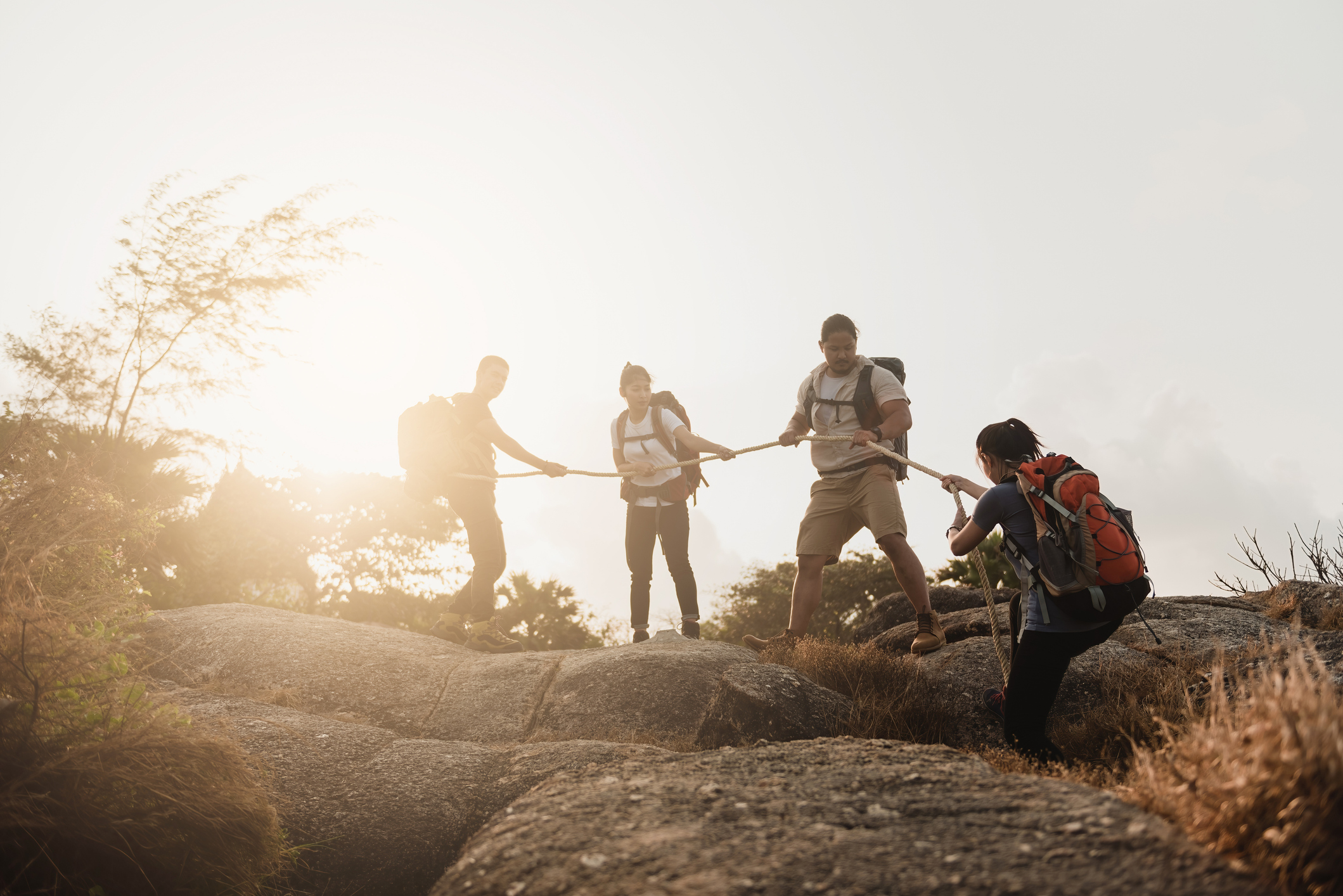 Four Asian and female climber groups, Backpacker, helping to pull the rope to support friends to the top of the hill, the concept of outdoor adventure activities.