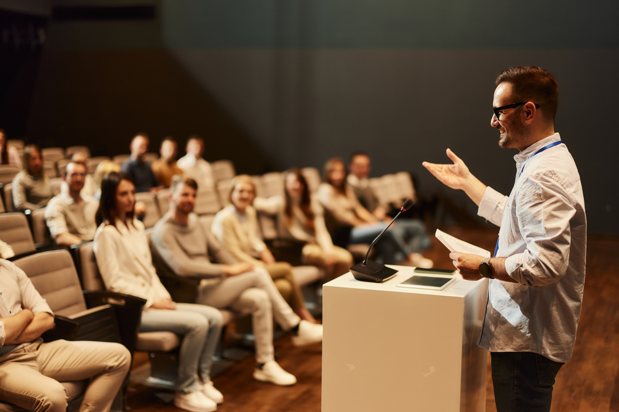 Happy businessman giving a speech in front of large group of his colleagues at convention center. Copy space.