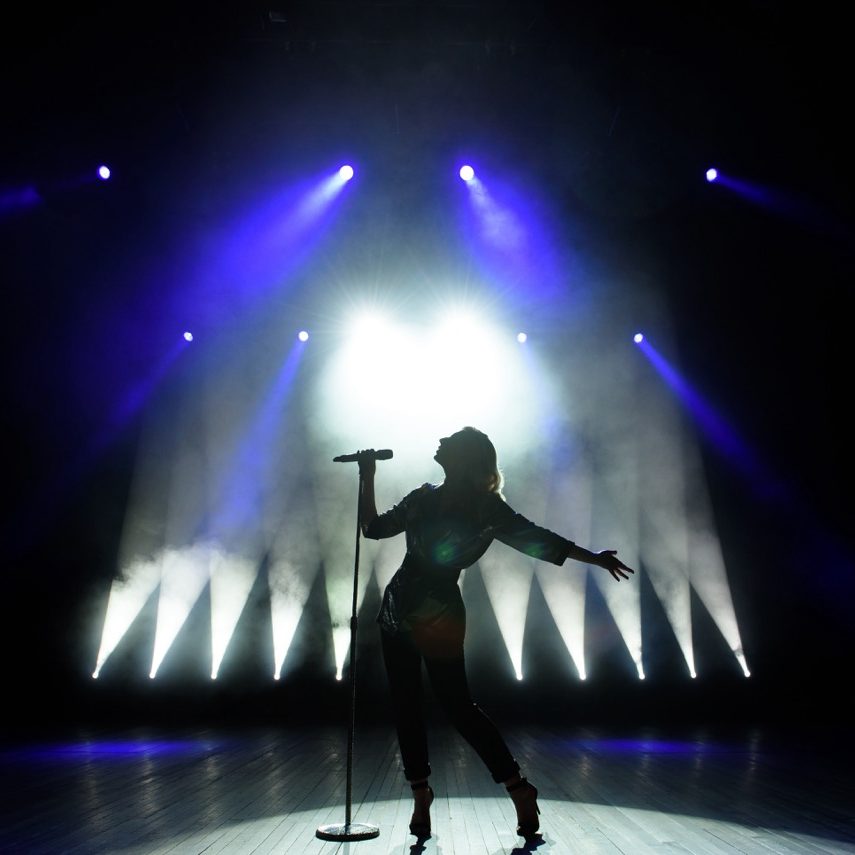 Silhouette of singer on stage. Dark background, smoke, spotlights